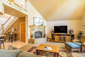 A spacious living room with a fireplace, a television, and a staircase leading to an upper level. - Charming 3 bedroom Stone Ridge Townhome (Sunriver)