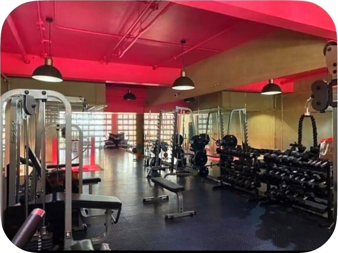 Une salle de sport équipée de divers appareils d’entraînement, notamment des machines de musculation, des bancs et des haltères.