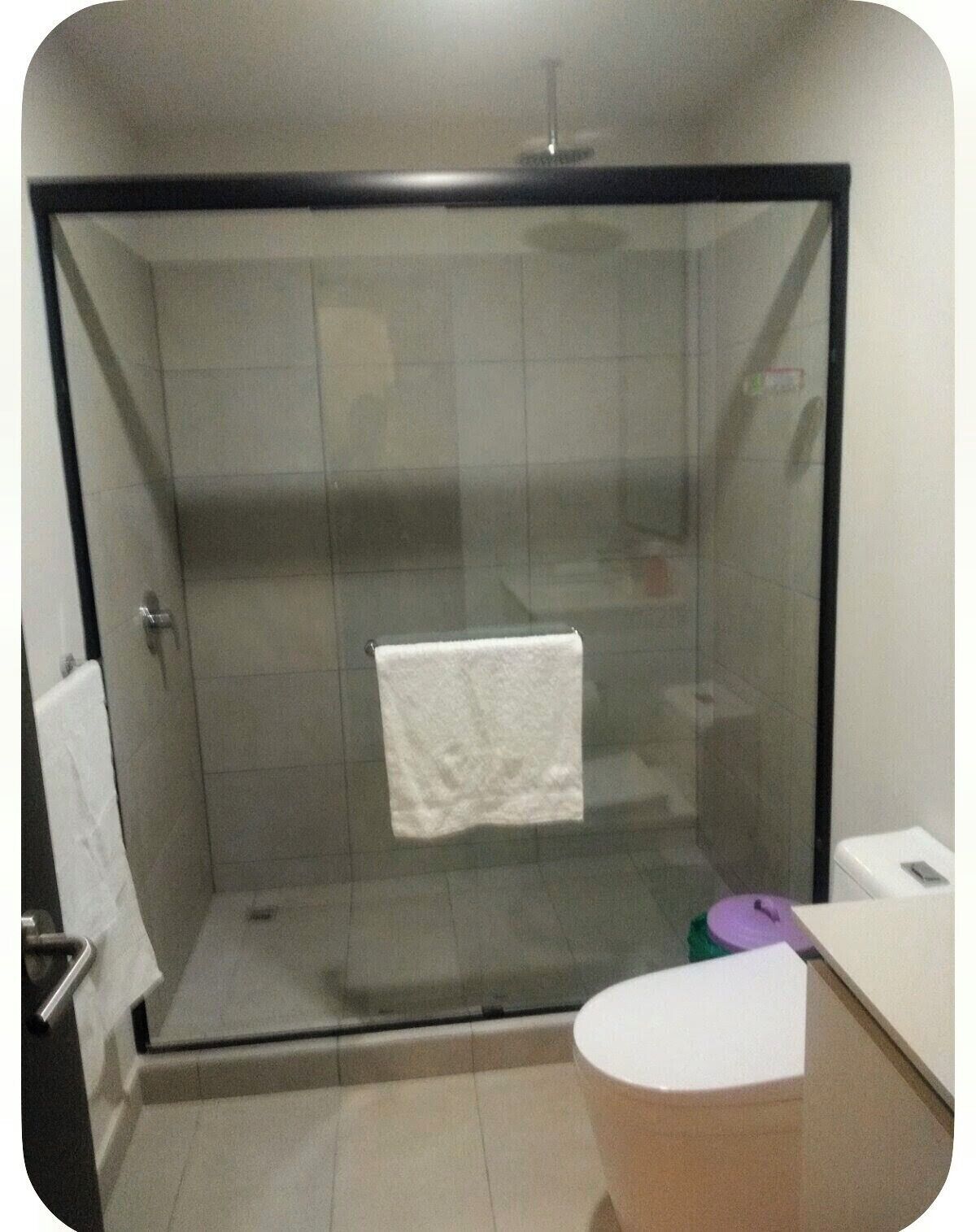 Een douchecabine met glazen wanden, een witte handdoek hangend aan de deur, een wit toilet en een klein, rond tafeltje.