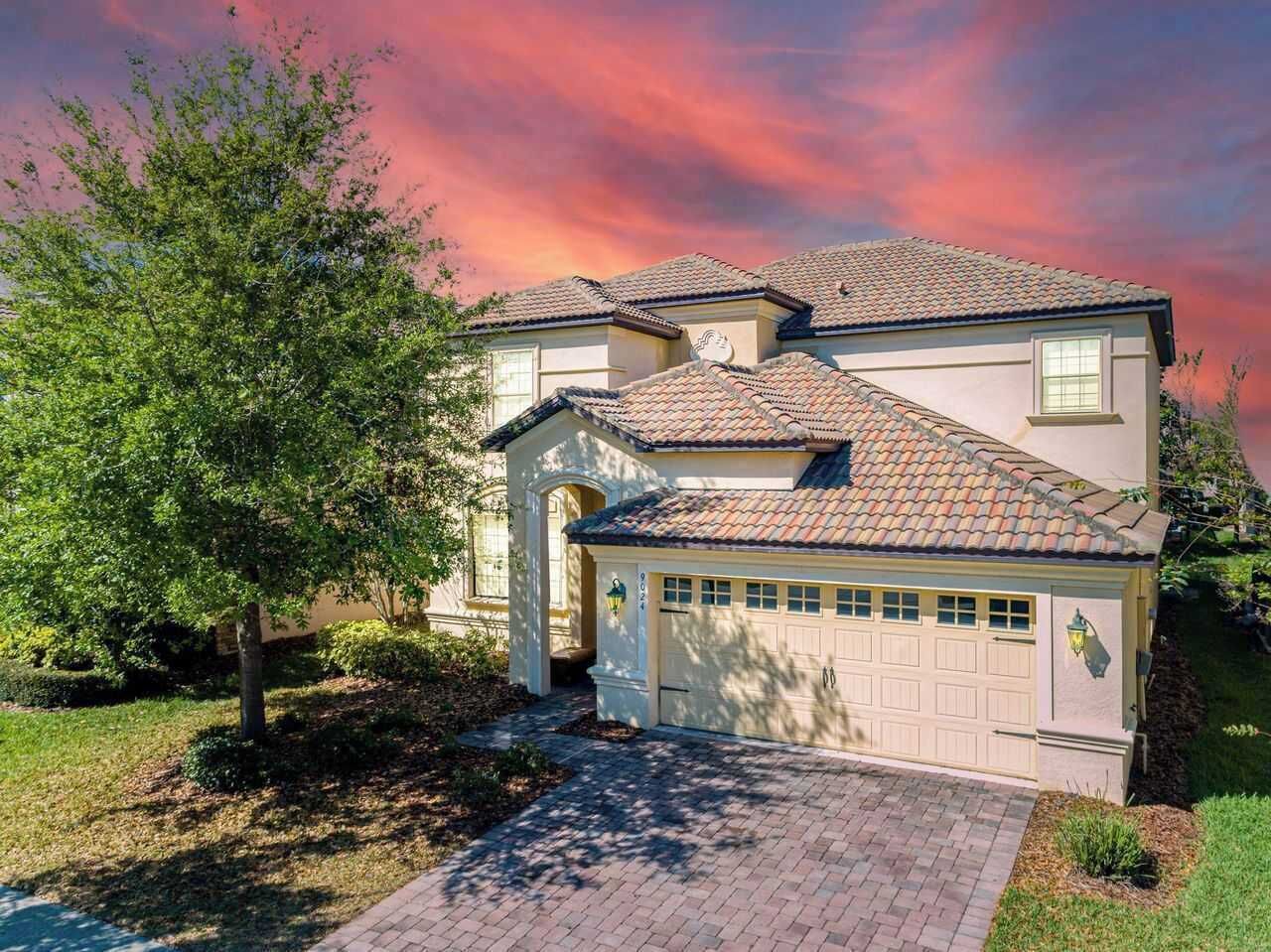A two-story house with a garage, a driveway, and a tree in the front yard.