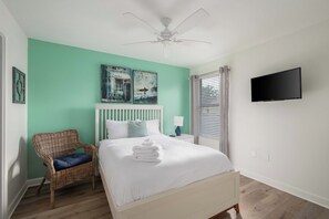 A bedroom with a bed, a wicker chair, a ceiling fan, a wall-mounted TV, and artwork. - 6Bedroom Luxury Pool Villa near Disney & Free Resort (Four Corners)