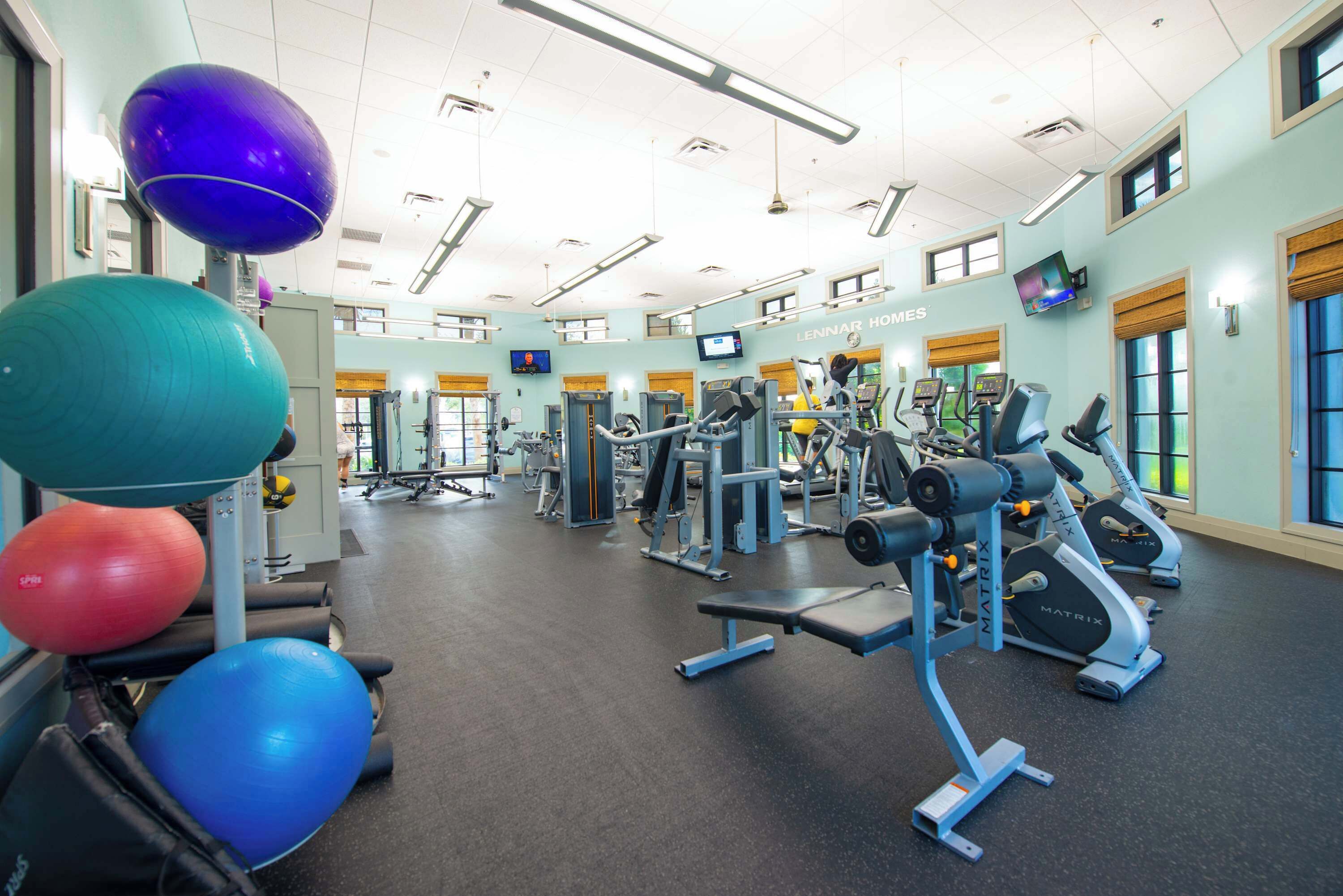 A gym with exercise equipment, a television, and a wall-mounted screen.