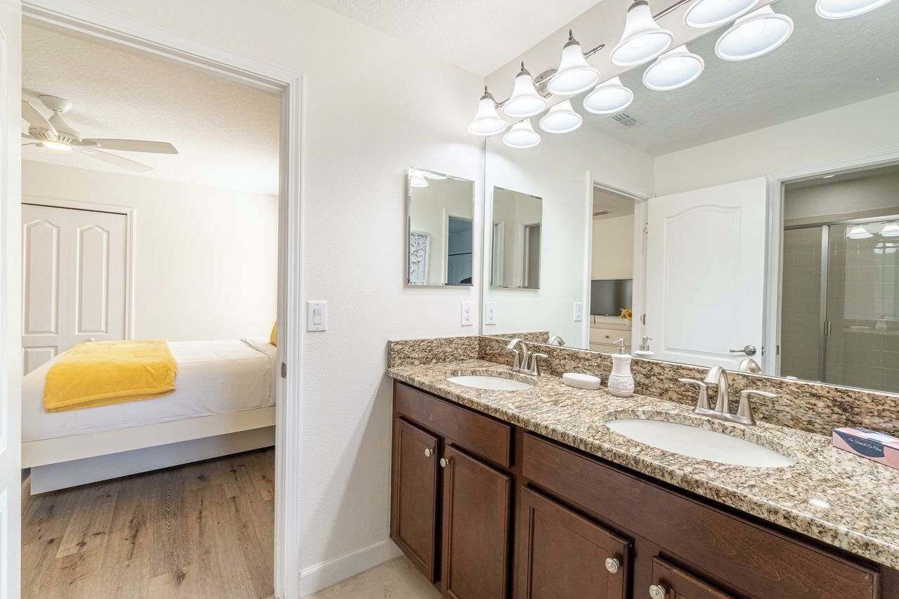 A bathroom with a double sink, a large mirror, and a ceiling fan.