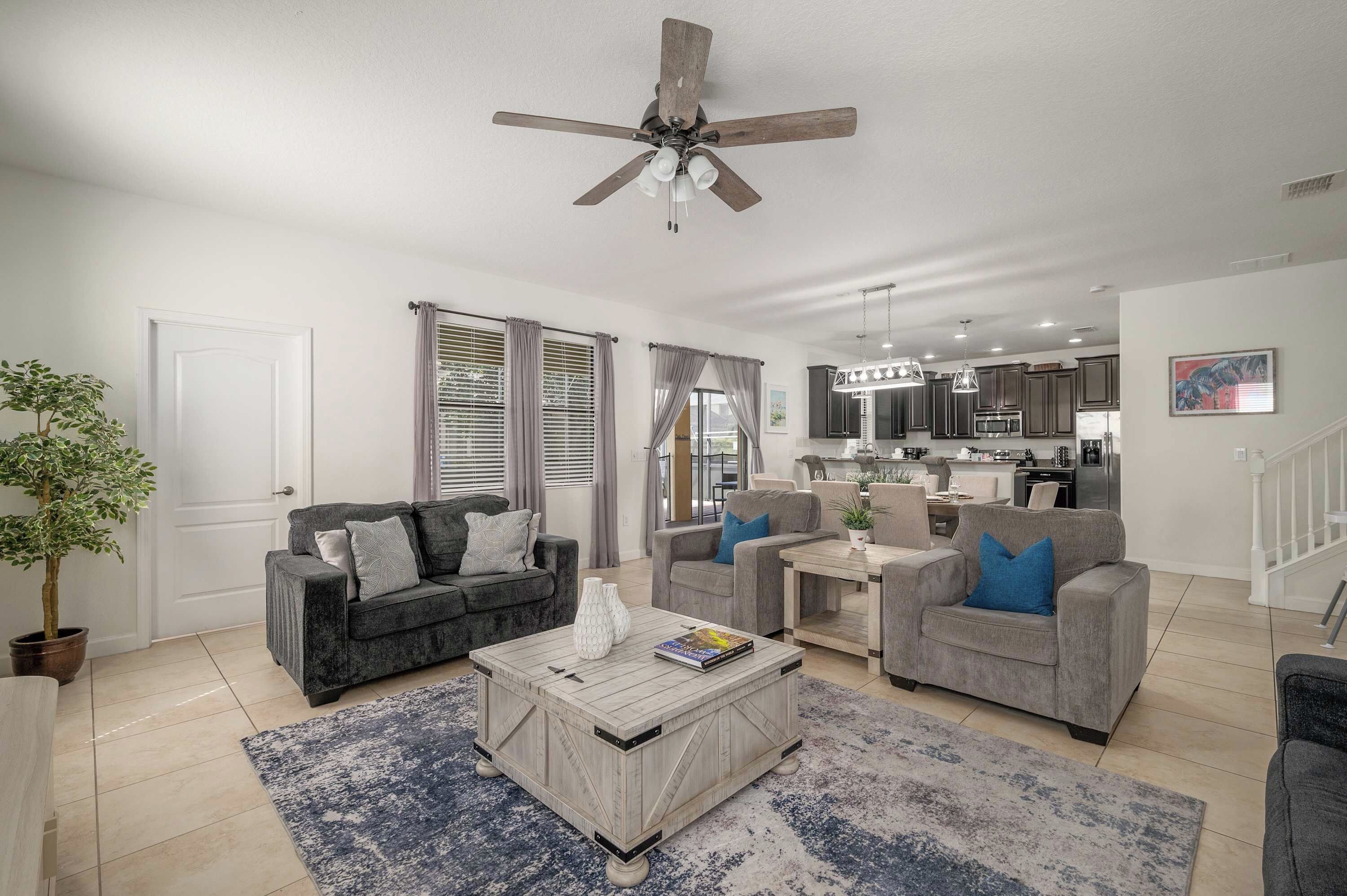 Un salon moderne avec un ventilateur de plafond, deux canapés, une table basse et une cuisine en arrière-plan.