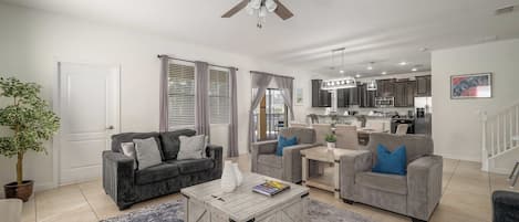 A modern living room with a ceiling fan, two sofas, a coffee table, and a kitchen in the background.