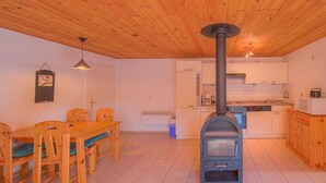 Ett kök med en vedspis, en matplats med bord och stolar samt en hängande lampa.