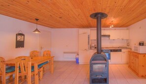 A kitchen with a wood stove, a dining area with a table and chairs, and a hanging light fixture. - Gemutlicher Doppelbungalow mit Terrasse im Ferienpark Mirow (Mirow)