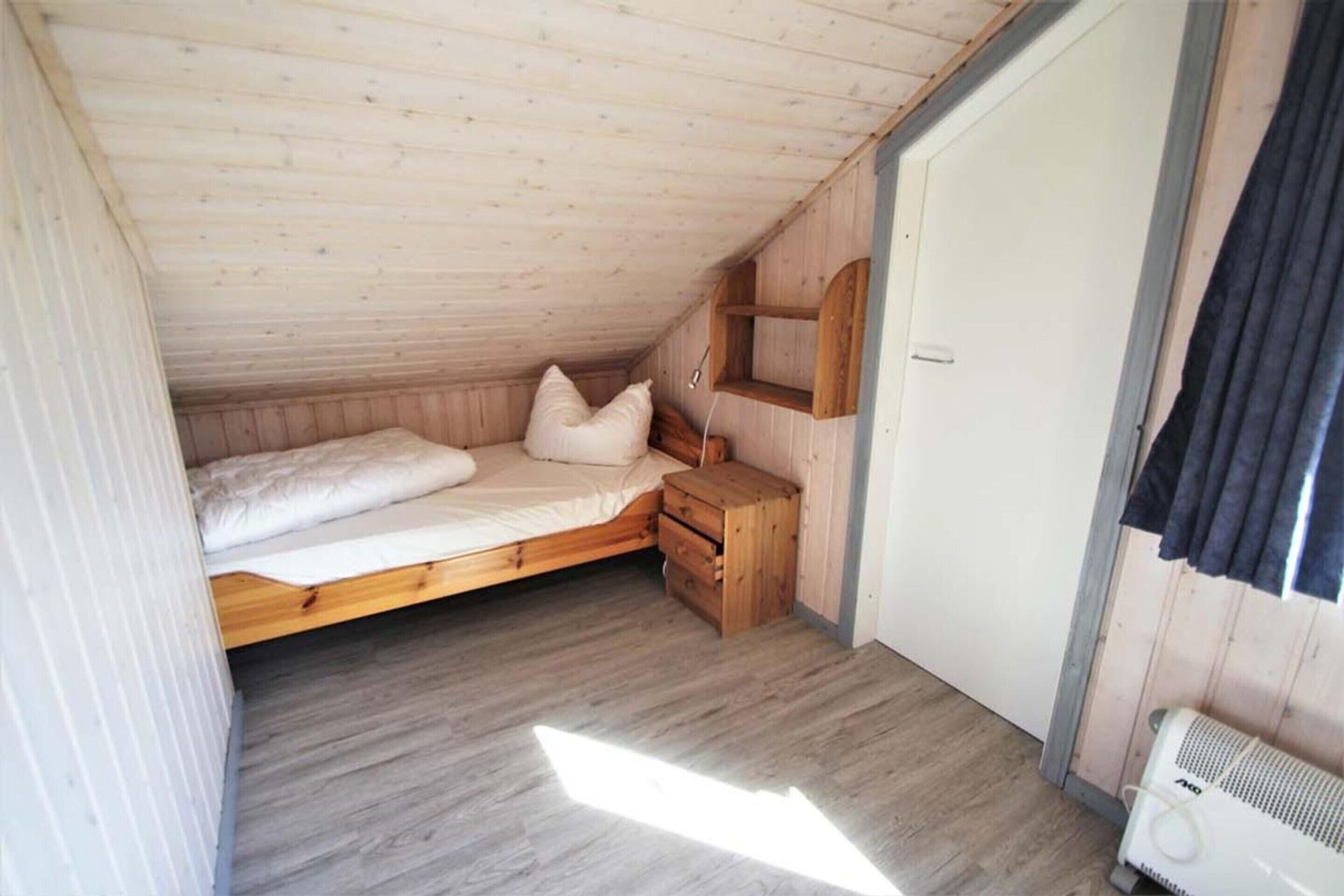 Een kleine eenpersoonskamer met een houten vloer, nachtkastje en een inbouwkast.