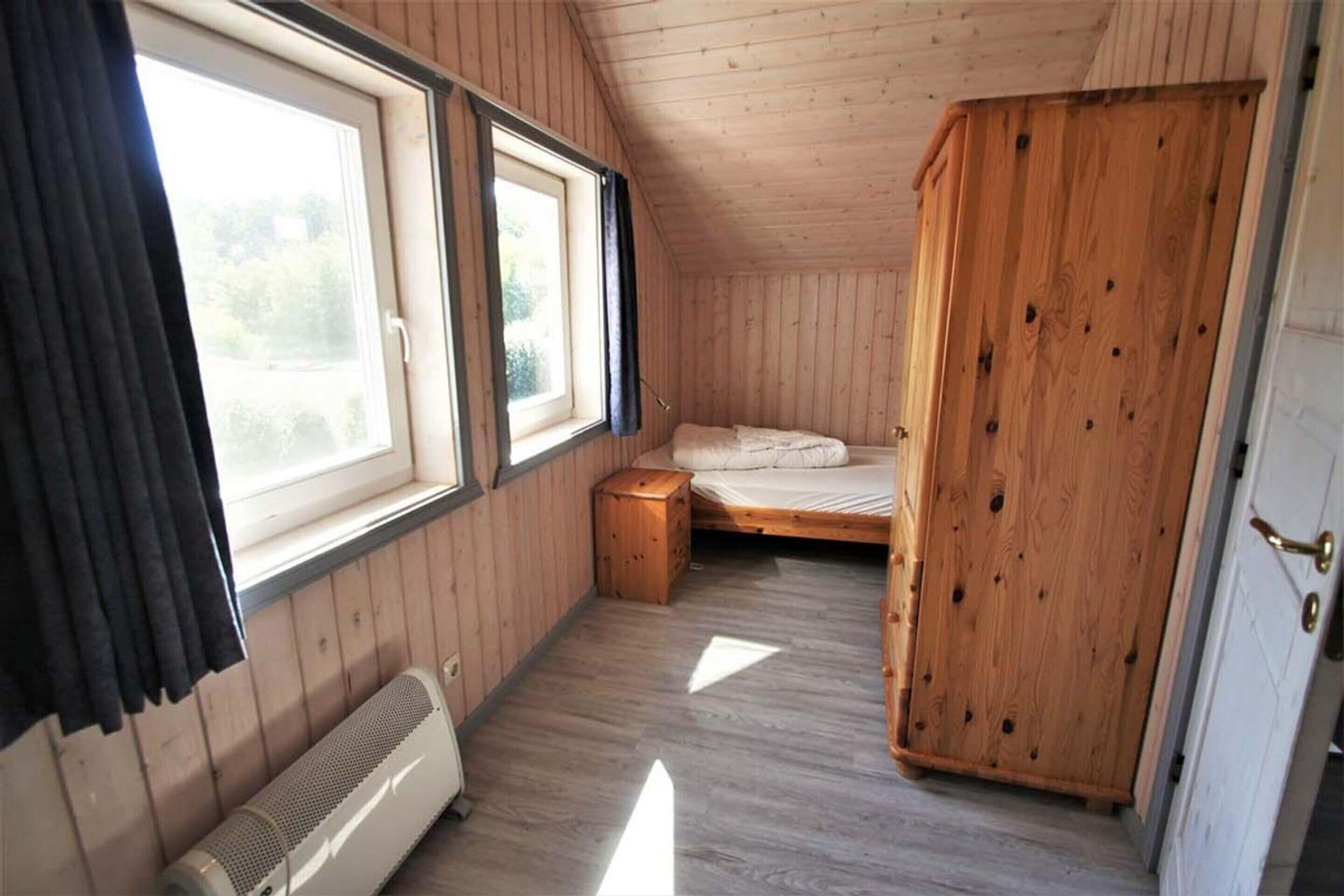A small, single-room cabin with a sloped ceiling, a bed, a wooden wardrobe, and a heater.