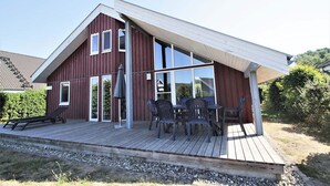 A modern house with a sloped roof, large windows, and a wooden deck with outdoor furniture. - Ferienhaus im Skandinavischen Stil mit Garten im Hafendorf Rechlin (Rechlin)