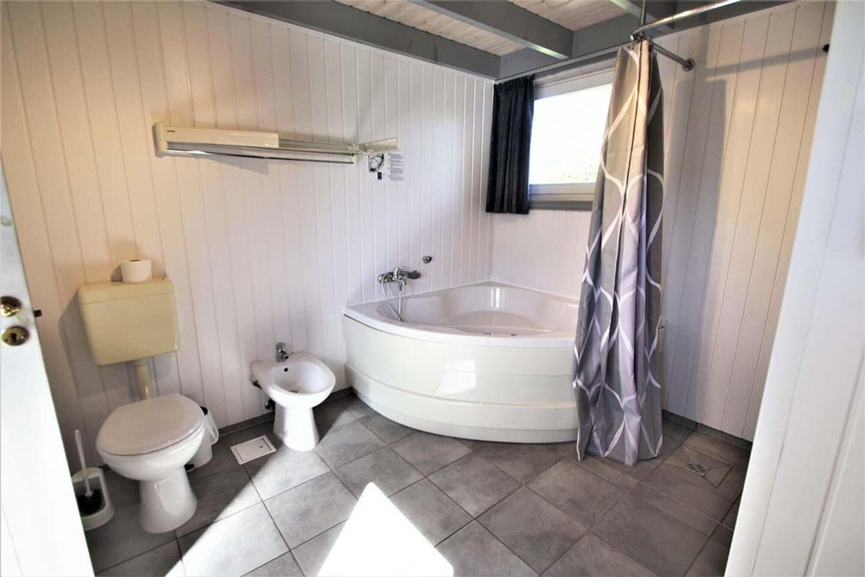 A bathroom with a bathtub, toilet, bidet, and a shower curtain.