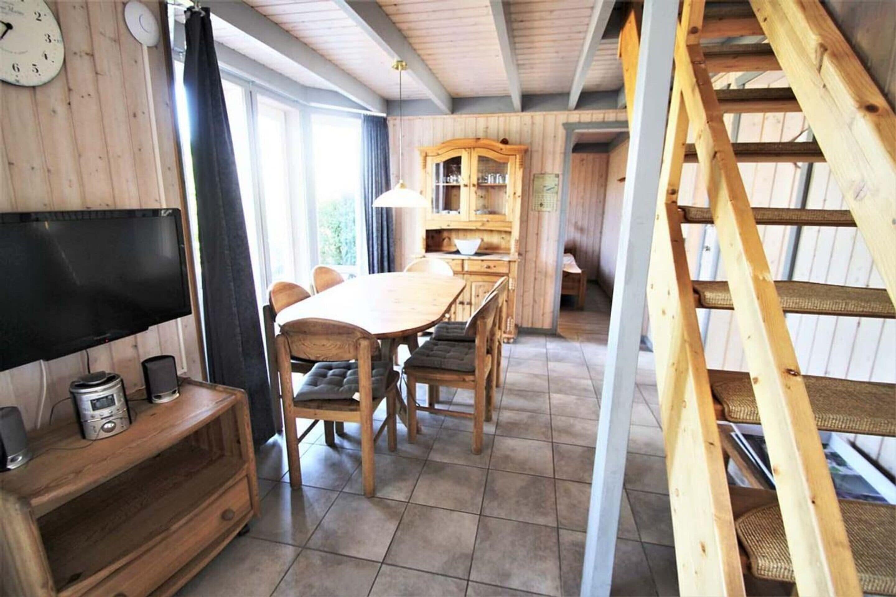 A wooden interior with a dining table, chairs, a television, and a staircase.