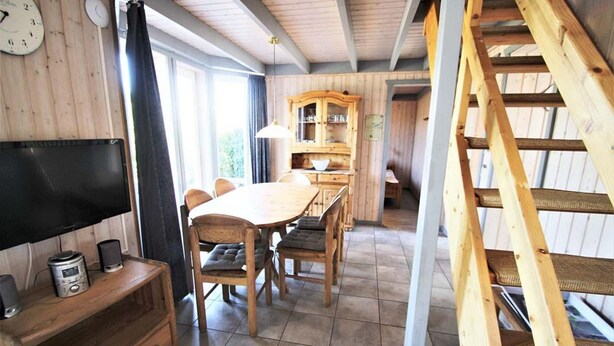 A wooden interior with a dining table, chairs, a television, and a staircase. - Ferienhaus im Skandinavischen Stil mit Garten im Hafendorf Rechlin (Rechlin)
