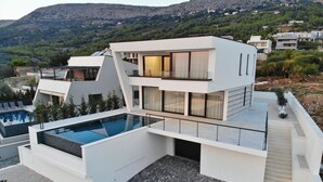 Et moderne hus med to etager, en pool på taget, store vinduer og et bjergrigt baggrundsmiljø.