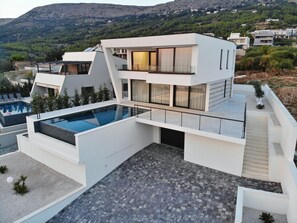 Ein modernes, zweistöckiges Haus mit Pool auf dem Dach, großen Fenstern und einer Bergkulisse.