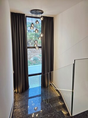 Ein zeitgemäßes Interieur mit Treppe, einer Pendelleuchte und Blick durch ein Fenster.