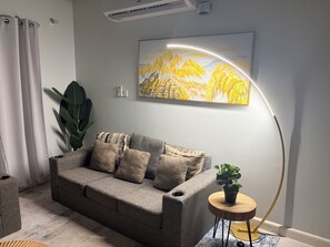 A living room with a grey sofa, a plant, a round wooden side table, a painting, and a floor lamp. - Fairway Retreat with beach access in Drax Hall (Saint Ann's Bay)
