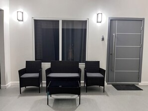 A room with three wicker chairs, a small table, a door, and two wall-mounted lights. - Fairway Retreat with beach access in Drax Hall (Saint Ann's Bay)