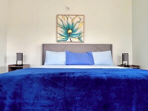 Hotellihuone, jossa on suuri sänky, pääty, kaksi yöpöytää ja seinälle kiinnitetty taideteos.