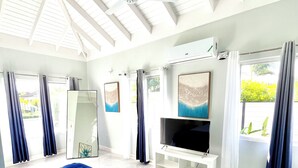 Een slaapkamer met een bed, een televisie, een plafondventilator en een raam met gordijnen.