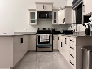 A modern kitchen with white cabinets, a stainless steel oven, a microwave, and a sink with utensils. - Fairway Retreat with beach access in Drax Hall (Saint Ann's Bay)