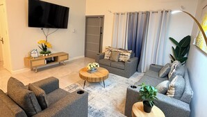 Een woonkamer met een bank, een bijzettafeltje, een televisie en een console met bloemen.