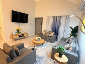 A living room with a sofa, a coffee table, a TV, and a console table with flowers. - Fairway Retreat with beach access in Drax Hall (Saint Ann's Bay)