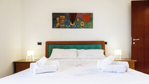 A neatly made bed with white linens and two rolled towels, a wooden headboard, a wall-mounted painting, and a wooden door. - Villino Boschetti—A terrace just 15 minutes from the beach in Vasto (Abruzzo)