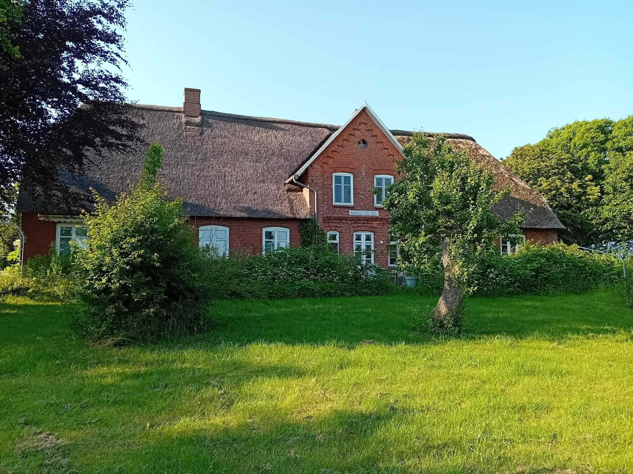 A large brick house with a thatched roof, surrounded by a well-maintained lawn and trees.