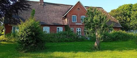 A large brick house with a thatched roof, surrounded by a well-maintained lawn and trees.