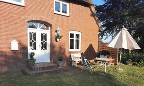 A brick house with a white door, a bench, a table, and a patio umbrella. - Charming vacation rental with garden access, about 4 km from the North Sea (Dagebüll) (Galmsbüll)