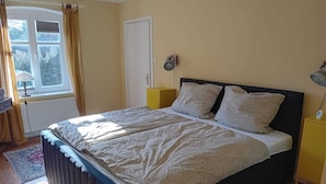 A bedroom with a bed, a window, a door, a bedside table, and a lamp. - Charming vacation rental with garden access, about 4 km from the North Sea (Dagebüll) (Galmsbüll)