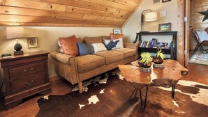 Una sala de estar acogedora con techo de madera, un sofá de cuero marrón, una mesa de centro de madera con plantas y un tapete de piel de vaca.