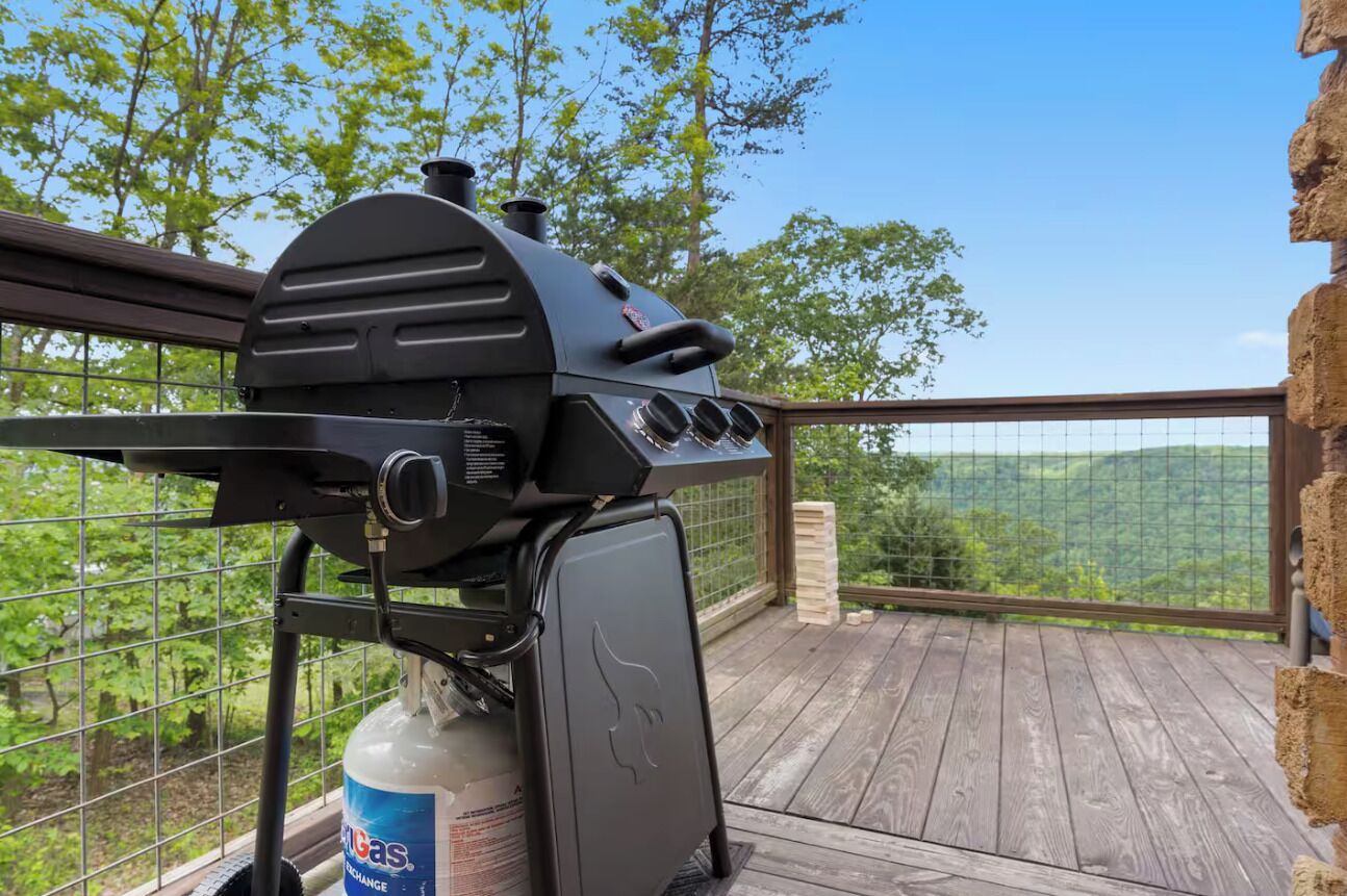 Ein Grill auf einer Holzterrasse mit Blick auf eine bewaldete Landschaft.