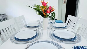 A dining table set with white plates, blue-rimmed glasses, and silverware, centered with a decorative plant. - Namo Villa Habaraduwa (Habaraduwa)