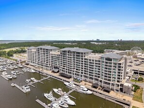 A marina with multiple boats docked, a large hotel building with balconies, and a Ferris wheel in the background. -  One of The Wharf's Newest Vacation Rentals. (Orange Beach)