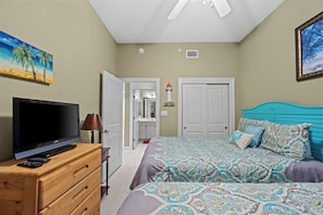 A bedroom with a TV, wooden dresser, patterned bed, and a painting of a beach scene. -  One of The Wharf's Newest Vacation Rentals. (Orange Beach)