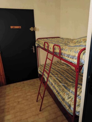 A bunk bed with a floral-patterned mattress, a black door with a handle, and a wooden floor. - Lagon Azur – Charmant studio avec piscine proche plage (Le Grau-du-Roi)