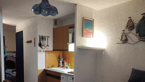 Ett kompakt bostadsutrymme med ett litet kök, tvättmaskin, matplats och en soffa med ett mönstrat kuddöverdrag.