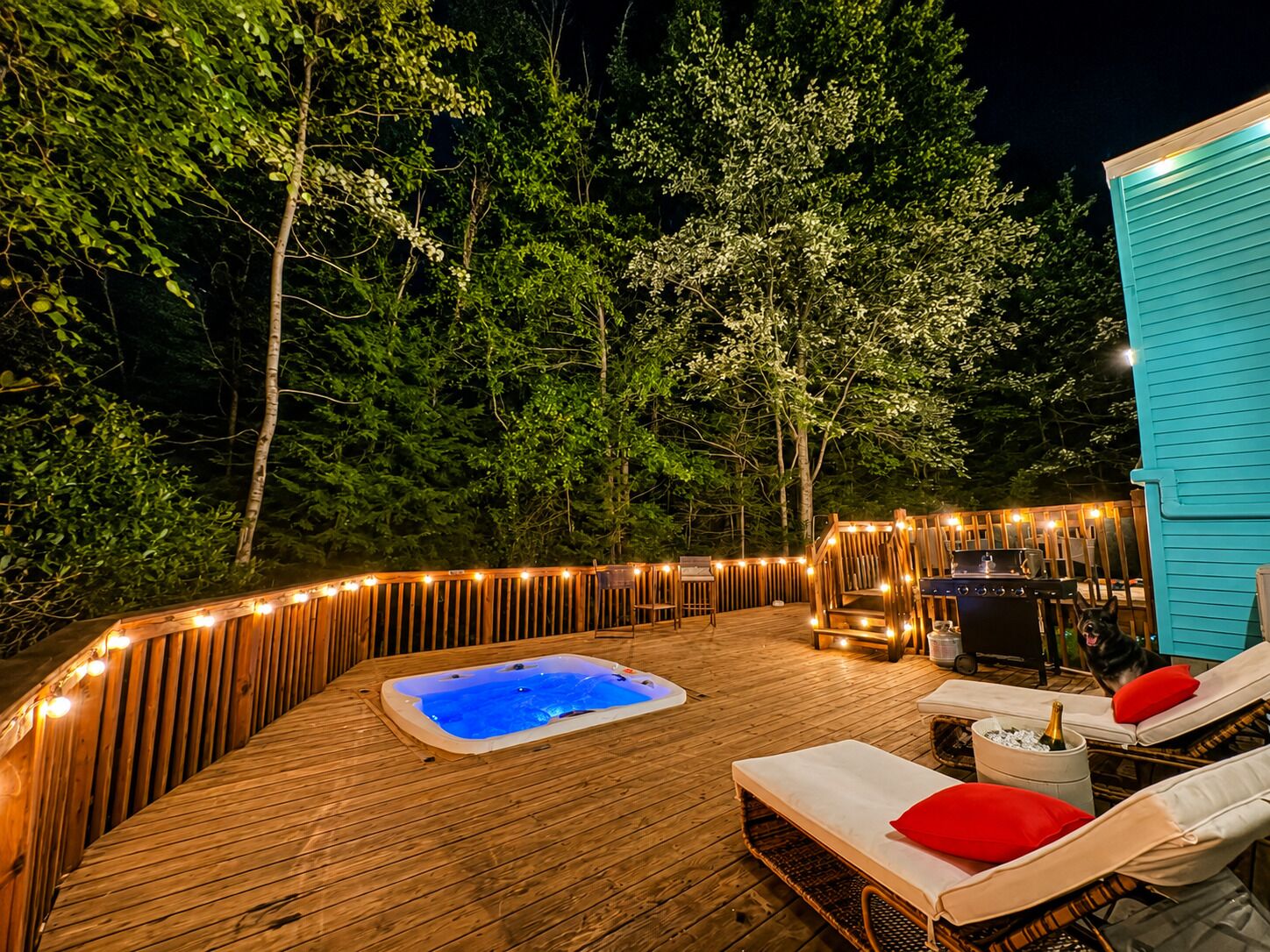 A wooden deck with a hot tub, lounge chairs, and a barbecue area, surrounded by trees.