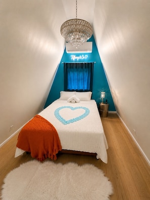 Ein Schlafzimmer mit einem Bett, einer Chandelier, einer Neonreklame und einem blauen Vorhang.