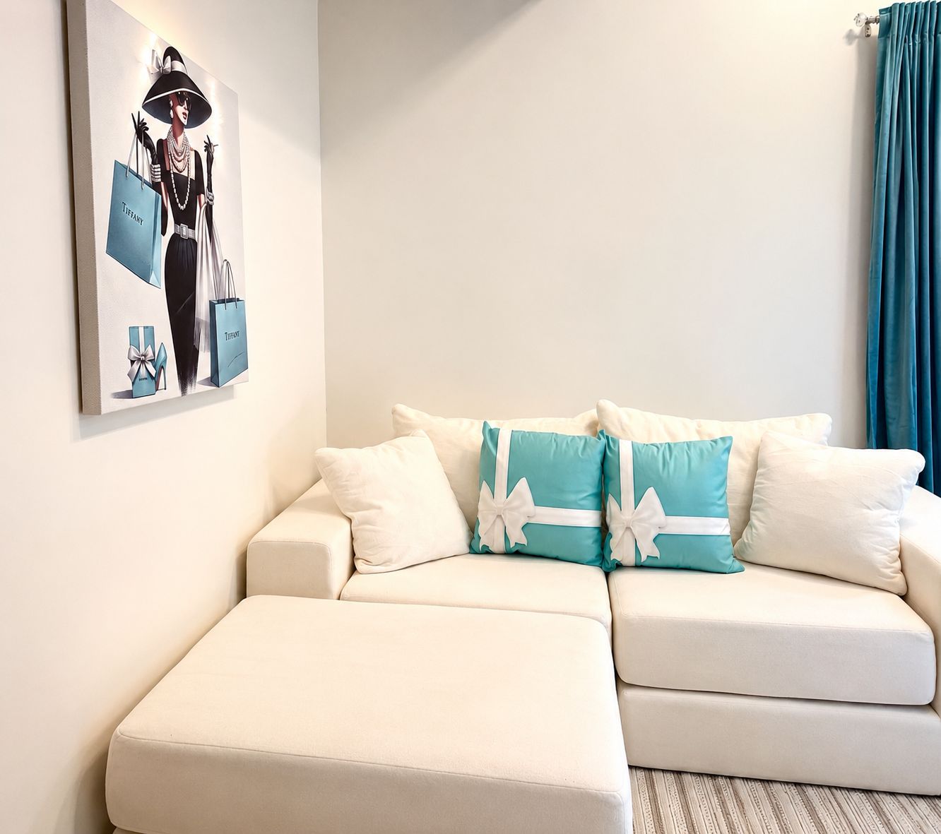 A white sofa with teal and white cushions, a framed picture on the wall, and a teal curtain.