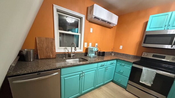Una cocina con lavavajillas, fregadero, estufa y armarios color turquesa.
