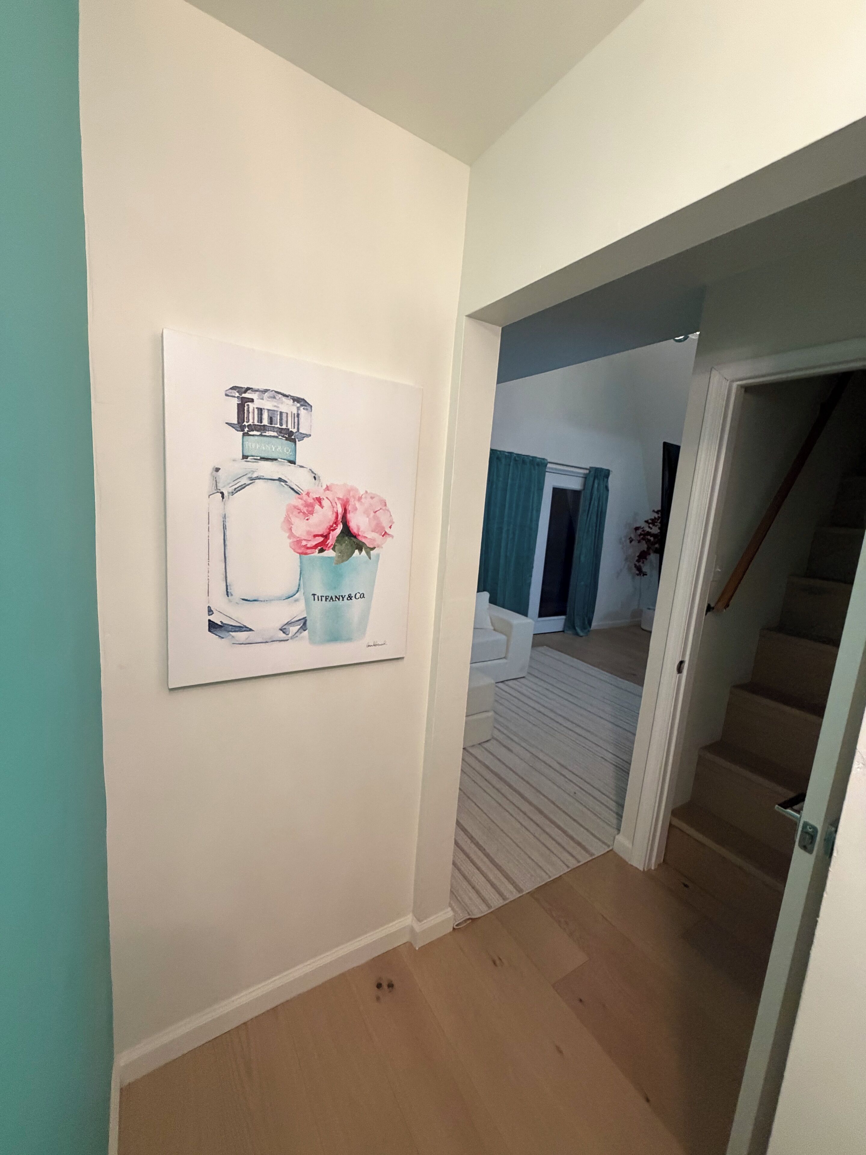 A hallway with a framed artwork of a bottle and flowers, a staircase, and a door leading to another room.
