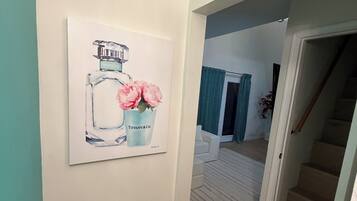 A hallway with a framed artwork of a bottle and flowers, a staircase, and a door leading to another room.