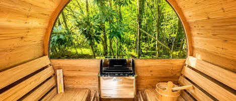 A sauna with wooden walls, a bench, a stove, and a window with a view of greenery.