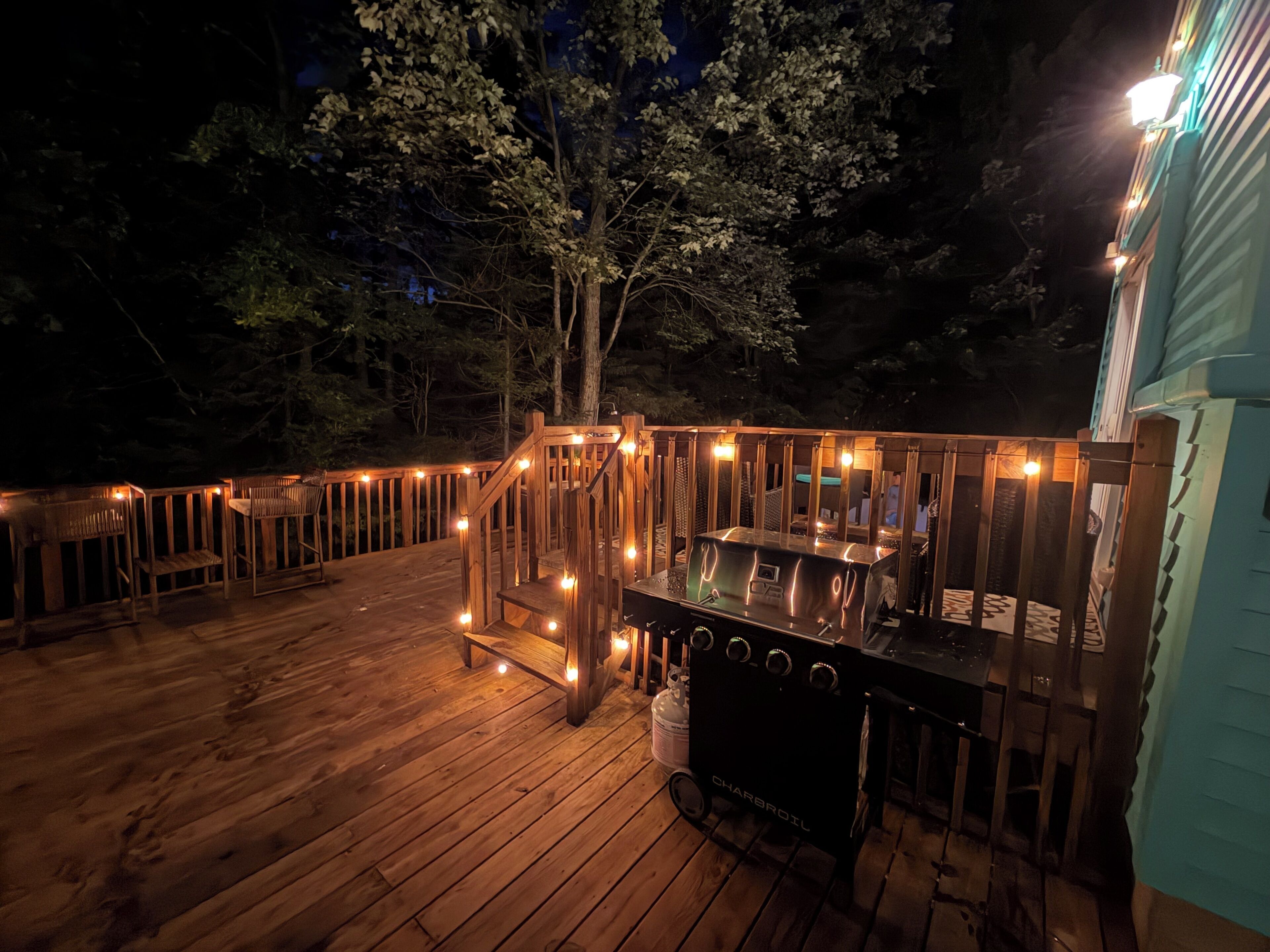 A wooden deck with a barbecue grill and string lights.