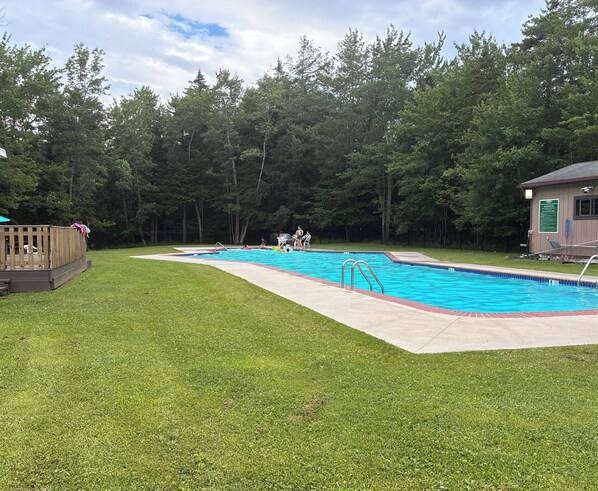 Una piscina con una terraza de madera y un edificio pequeño al fondo.