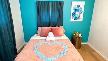 Un dormitorio con cama, decoración en forma de corazón sobre el edredón, una araña y una pared con detalles azules.