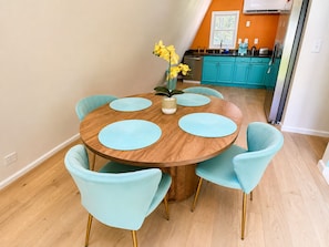 Un coin repas avec une table ronde en bois, six chaises bleu clair et un vase rempli de fleurs jaunes.